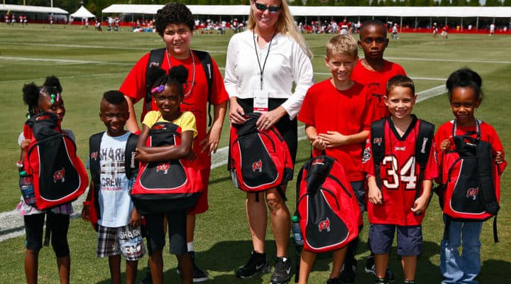 A DEX team member with kids holding donated backpacks at a youth sports event